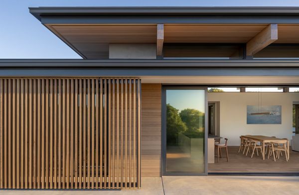 The wood screens slide beneath the deep roof overhang, introducing a flexible layer that shapes light, privacy, and the home’s relationship to the landscape.