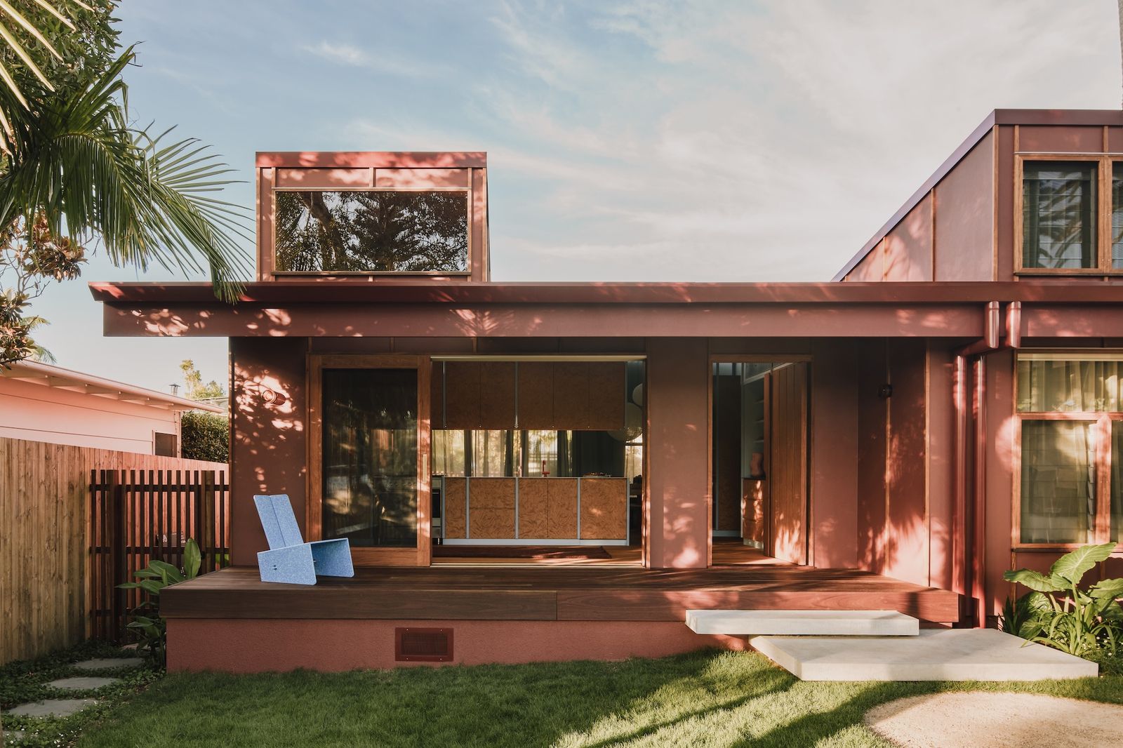 The James Hardie Fine Textured cladding is painted Dulux Reddy Brown, while the timber sliding doors and windows are by East Point Joinery. A Lani Lounge chair by Potato & Sprout sits on the deck.