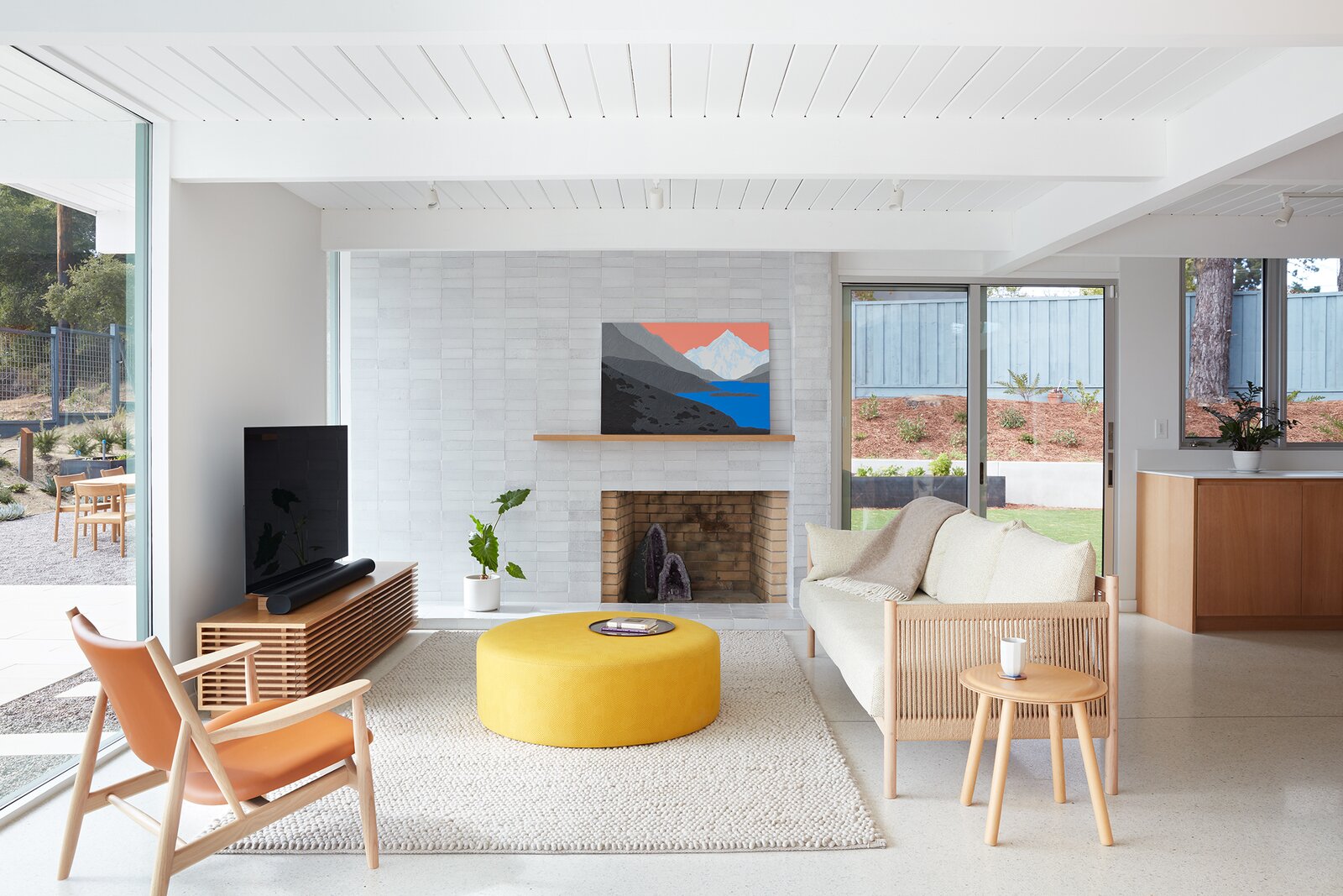 The living area retains the home's original fireplace and masonry wall, with new sliding doors next to the kitchen that connect to the side yard. The sofa and side chair are from Ariake, the ottoman table from Hem, and the rug is from Hay.