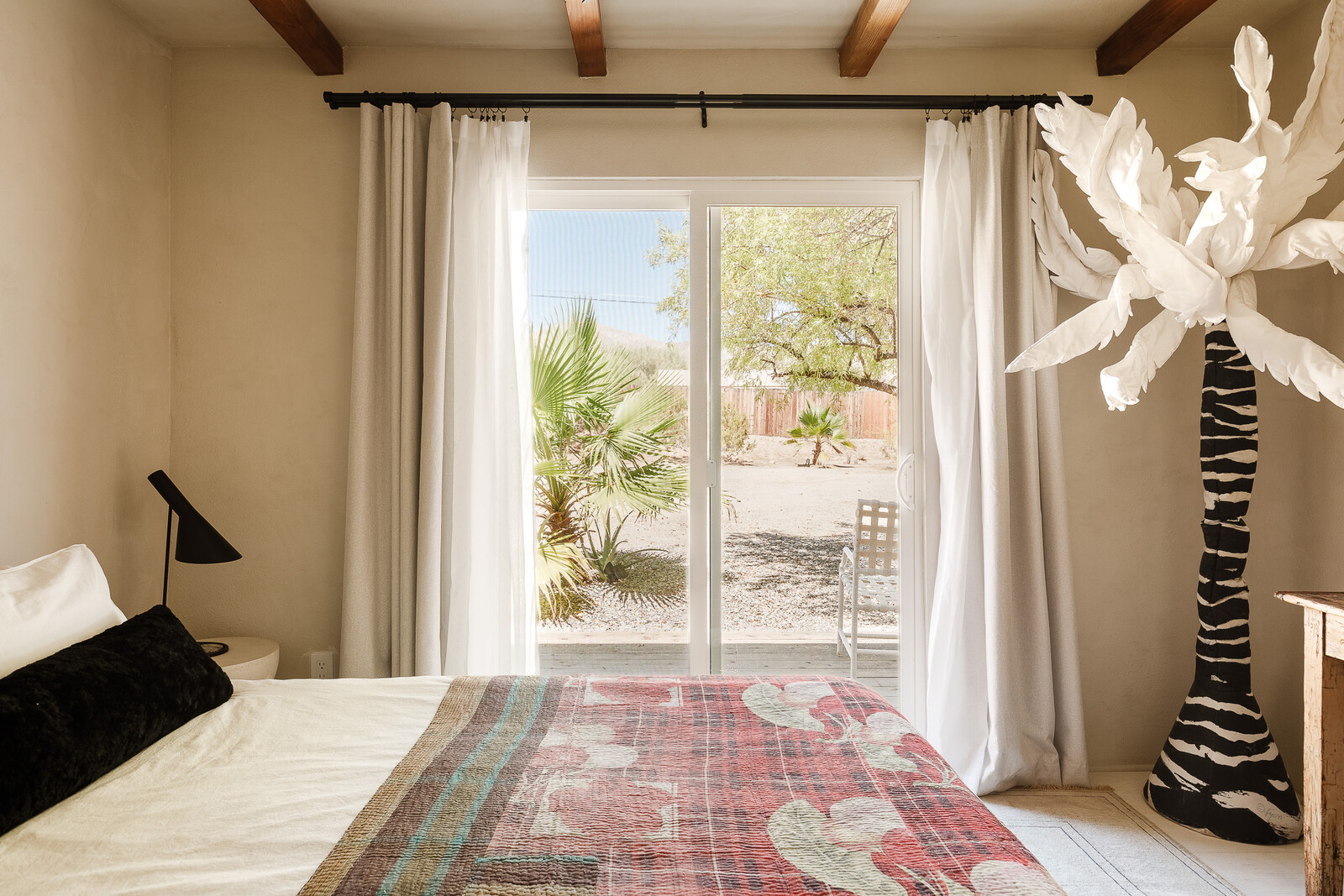 The updated guest room features a sliding glass door, which was repurposed from its original location off the kitchen. The vintage 1980s palm tree soft sculpture was sourced by Jonathan Pessin.