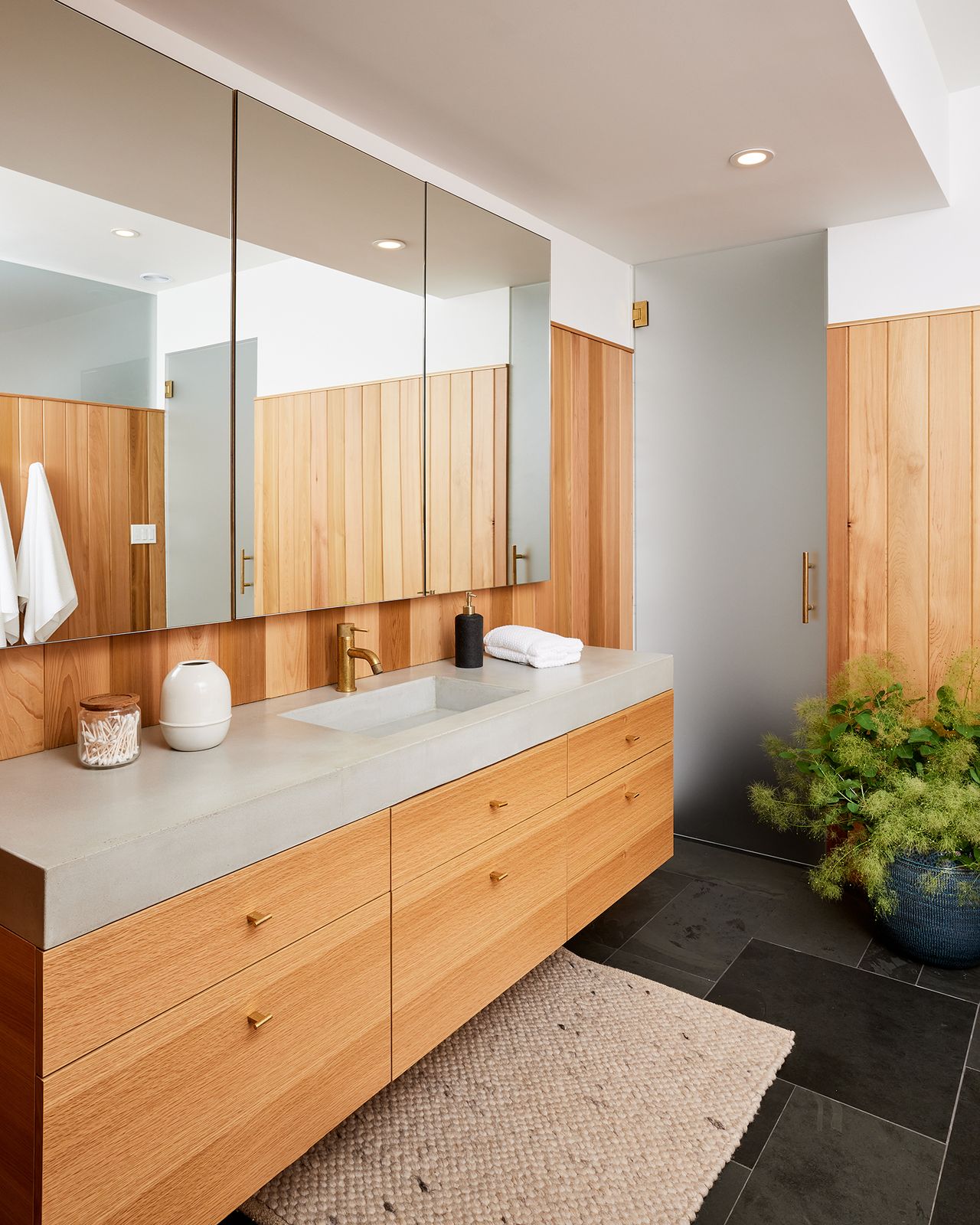 In the primary bath, cedar wall paneling complements an oak vanity with a custom concrete sink and counter. The floors are slate tiles by Cle.
