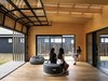 Modern home with Living Room, Bench, Concrete Floor, Chair, Plywood Floor, Stools, Medium Hardwood Floor, Ceiling Lighting, Ottomans, Light Hardwood Floor, Sofa, and Painted Wood Floor. The Outdoor Room is an open inbetween space filled with light through the large roller door and clear battened roofing above. It was designed from a need to reflect the essence of the relaxed "kiwi-bach" of impromptu gatherings, and spontaneous accommodations for family and friends. Photo 4 of The Crest House
