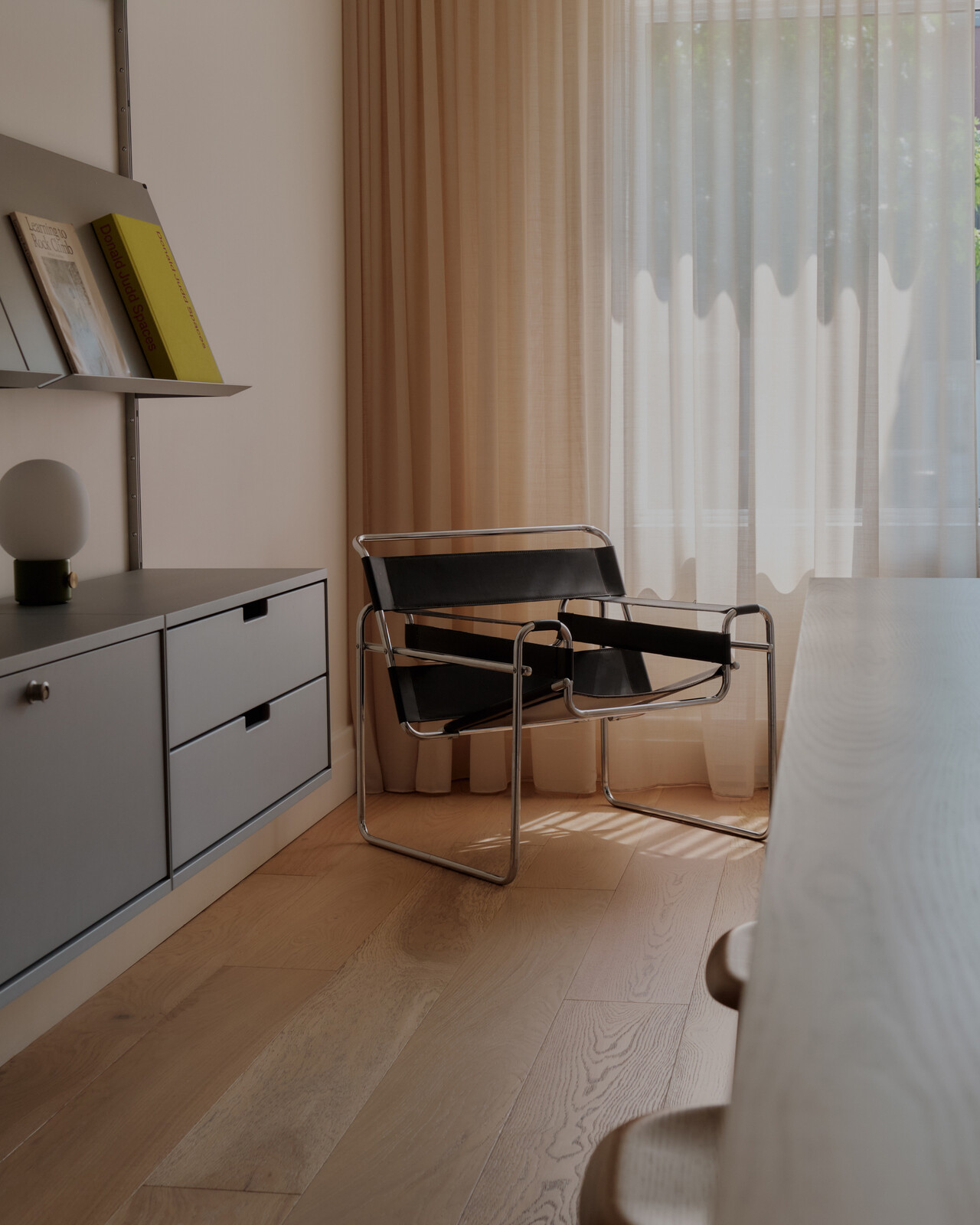 A vintage Wassily chair sits in the library by the soft, butter-colored curtains. 