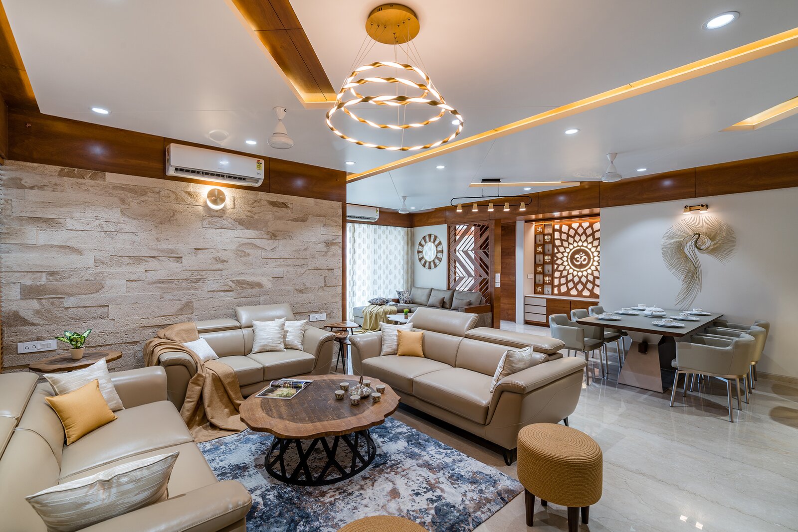 The drawing room is characterized by bespoke furniture in hushed tones. Neutral sofas, patterned rug, and ornate puffies embellished with raw-wood center table are highlighted with brick-patterned wall cladding.