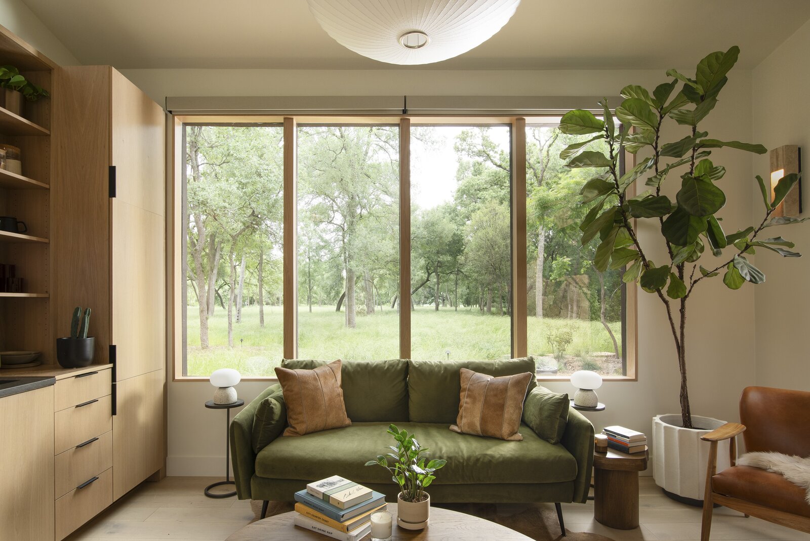 A sitting area features a sofa from Edloe Finch, a Herman Miller Nelson Saucer Bubble Pendant, and a Troubadour Saddle Leather Wood Frame Chair from CB2. 