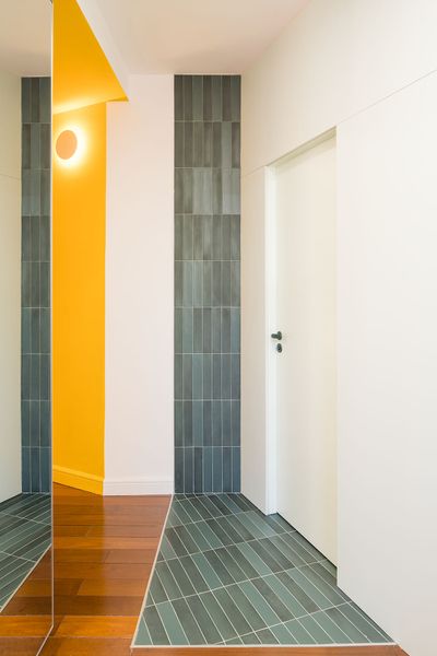 A blue partition marks the living area, red shutters bring in light and air, and green tile forms a threshold from the bedroom into the en suite bath.