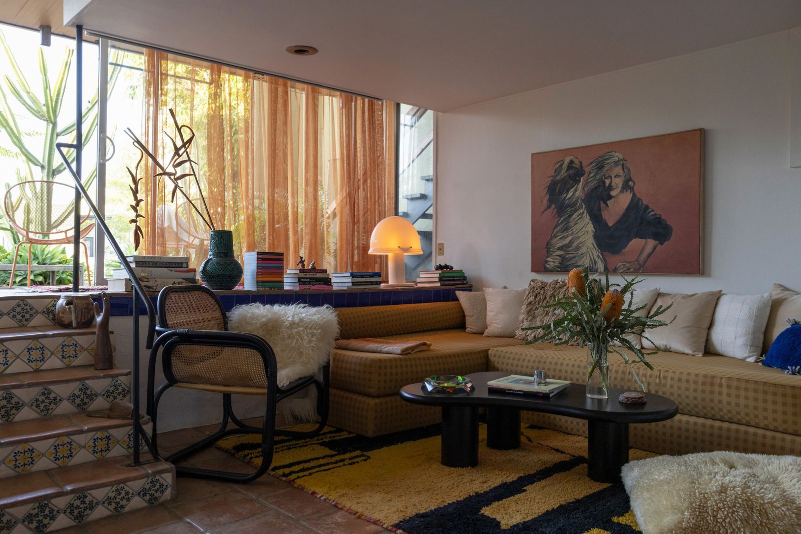 The home embraces indoor-outdoor living with a large sliding door that serves as its only window. A living room couch by HUBBA HUBBA (made of mattresses and upholstered fabric) wraps around a TOV Furniture coffee table, anchored by a custom Moroccan rug found on Etsy. The ashtray is by Fundamental Berlin and the mushroom lamp is by Rodolfo Bonetto for Iguzzini.   
