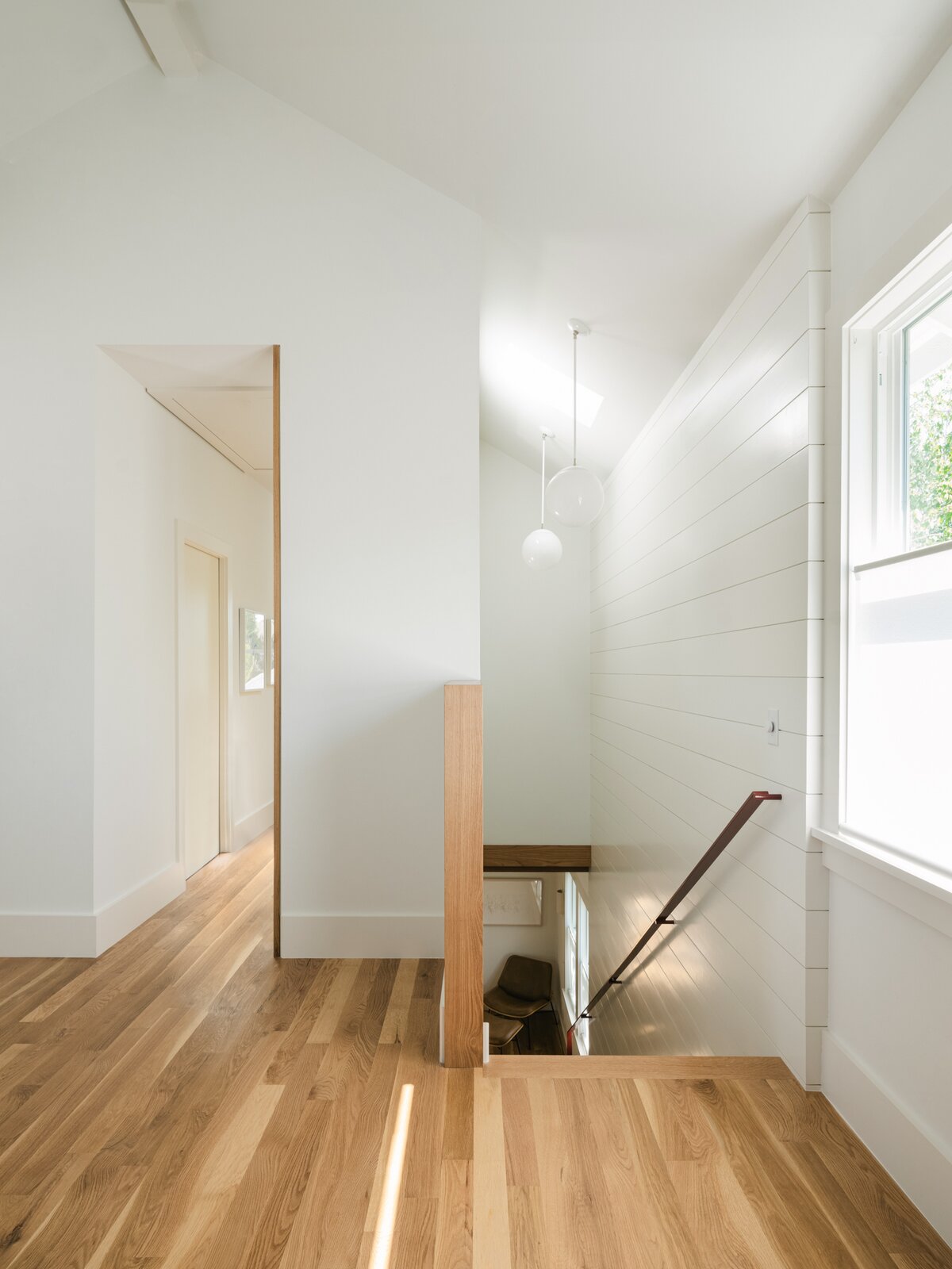 To create a visual connection between the two sections of the house, Janusz used white-painted shiplap, oak flooring, and globe-shaped pendants in each. Refined details, such as vertical oak trim in the hallway, elevate the project's feel. "I thought it was important to mark transitional spaces,