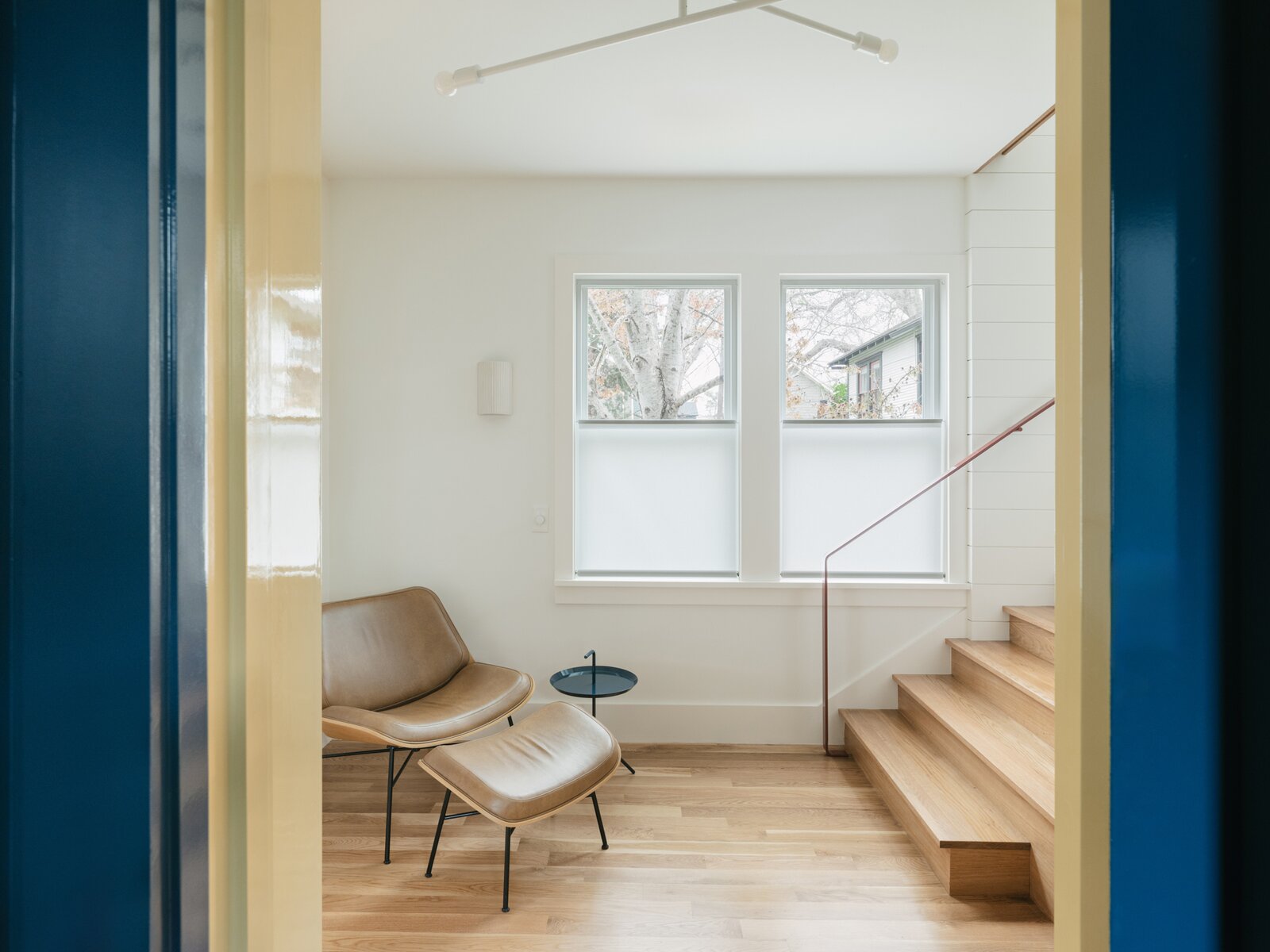 A bent-steel stair railing, painted with Frank Lloyd Wright's Fallingwater Red, brings a jolt of energetic color to the neutral gallery space below the primary suite. "We put a chair oversized hallway for lounging and reading,