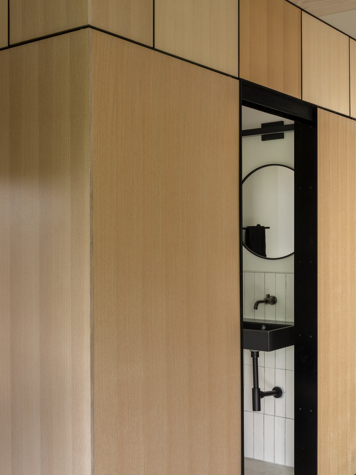 Black accents ground the light wood wall paneling, and the vertically installed subway tile adds texture to a peek-a-boo bathroom.