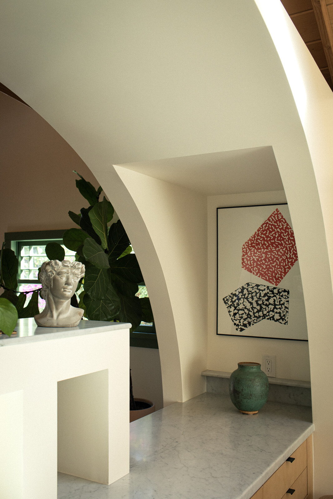 A print by Kyla Chevrier hangs in a niche between the kitchen and dining area. A marble slab tops IKEA cabinetry fronted with Plykea doors.