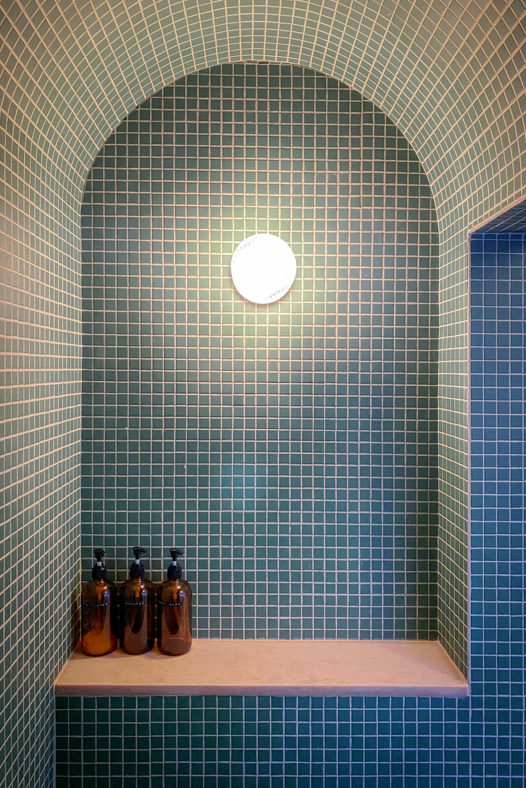 A blast of blue continues the tile-forward motif of the bathroom with Daltile's Keystone in Emerald Green. The bench's salvaged marble slab is a close color match to the pink tile backing the sink, and the sconce is RBW.