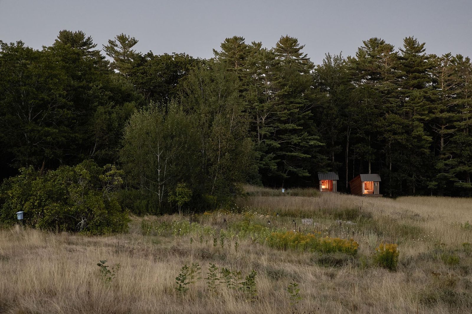 The tiny, open sleeping shelters abut a stand of woods. Their open fronts frame views of the Wanderwood farm. 
