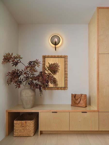 A utilitarian entryway featuring birch cabinetry is softened with an earthenware vase and an ornate mirror. White oak flooring spans the home. 