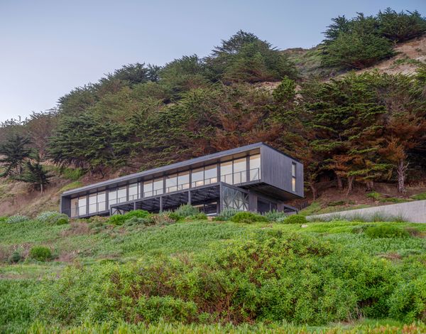 The house is set on a small clearing in a cypress-filled hill that slopes steeply down to the Pacific Ocean

