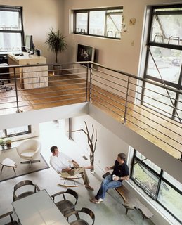 The open office and bedroom reside on either side of the second story catwalk. Below, Walz rests on a George Nakashima–inspired bench designed by architect Harry Levine’s Uncle Murray, while industrial designer Scott Summitt sits in a vintage Eames rocker.