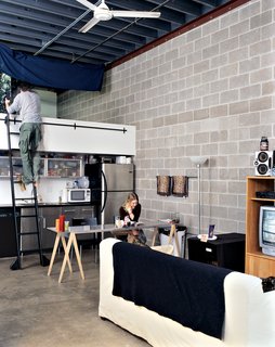 Sleeping space is adventurously tucked away in an alcove above the kitchen, accessible by a track ladder that slides along a rail mounted above the counter.