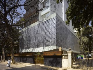A Modern Aesthetic in Mumbai - Photo 6 of 17 - A view from the street reveals the front and side elevations of the building, with somewhat of an architectural refrain of perforations running up the side of the apartments. The balconies, made from a recycled Indian railway hardwood, employ closely linked slats whose gaps widen as they go up, to allow breeze and light in. To their right are the apartments' bedrooms.