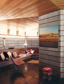 A concrete-block wall and a built-in bench line the living room, where a photo by Robbins and a painting by Barry McGee hang near a Catenary chair by George Nelson.