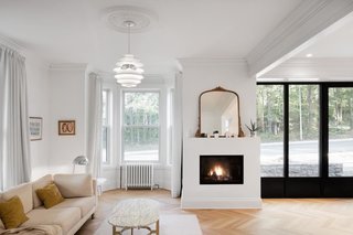 "The ceiling moldings were kept to create a sense of intimacy, and to blend the home’s classical style with the modern look of the kitchen," architect Maxime Moreau says. A PH Snowball light pendant by Louis Poulsen illuminates the living room, and a gas fireplace by Foyer Universel keeps it warm, with a mirror above the fireplace allowing light to bounce around the space.