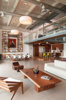 A Miami Renovation That Blends Concrete and Rich Wooden Interiors - Photo 2 of 7 - A row of Nahtrang pendant lights creates an axis, anchored by the enormous custom bookcase framing the dining room artwork. The seating at lower left is the ASA Armchair by Bernardo Senna; the dining table charis are by Martin Ballendat for Anima Domus.