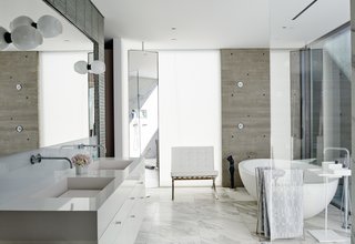 Milk-glass sconces by Lindsey Adelman are mounted on the master-bathroom mirror over a custom vanity with a Cosentino quartz-composite countertop. The freestanding Po bathtub by Boffi sits on a floor of Calacatta Gold marble.