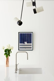 In the kitchen, a Dornbracht faucet joins a Silestone countertop. Paint in All White by Farrow & Ball—a shade used throughout the house—provides a crisp backdrop for a print from Thomas Demand’s series The Dailies, while a vintage Boris Lacroix lamp hangs ready to illuminate the scene.