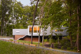 Built on a challenging hillside site and tucked behind a thicket of trees, the Bridgman, Michigan, house designed by Scott Rappe provides a modern weekend retreat for a Chicago couple. "One of my first responsibilities was getting the owners up to their house and essentially on one level. Because of the pie-shaped property, we needed to push the building up the hill to provide square footage for the program. By keeping the building perpendicular to the slope, using piloti on one side and a retaining wall on the dune side, we were able to insert foundations with minimal disturbance," says Rappe.
