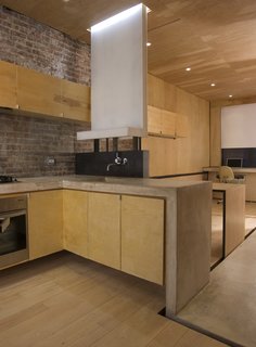 The apartment, measuring just over 400 square feet, opens into the kitchen, which architectural designer Alan Y. L. Chan outfitted with a Dornbracht faucet and a sink of his own design. The black steel backsplash doubles as the back of a built-in bench on the other side. A concrete "ribbon" serves as the main design concept and the countertop, and continues throughout the apartment. A built-in LG refrigerator is located just across the concrete floor at right. Image courtesy Brian Riley.