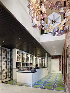 An installation by Kirsten Hassenfeld hangs above the custom reception desk, which is topped with slate. The floor tiles are 14OraItaliana's iGattipardi line. &Tradition makes the pendant lights and the Vivid Victorian wallpaper is from Flavor Paper.