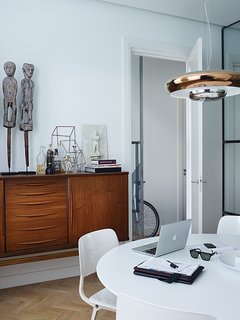 Nederhof purchased the vintage teak dresser from an online secondhand store. On it stand fertility statues and a miniature sculpture by Antonino Sciortino. The steel-framed glass doors fold back into the wall, and the space is oriented so clients can enter the office without traipsing through the entire flat.