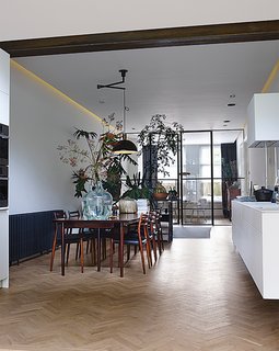 The living room, dining room, and kitchen are arranged in a 60-foot-long enfilade. The pendant light above the table is Nemo by Franco Albini for Cassina. A grouping of succulents and Monstera deliciosa plants act as a natural room divider.
