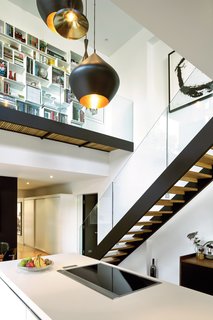 A Renovated Flat in Moshe Safdie's Habitat '67 - Photo 2 of 8 - The couple’s white Bulthaup kitchen is set within a double-height volume hung with Tom Dixon Beat lights, arranged in a custom configuration by interior designer Maria Rosa Di Ioia. Overhead, Cubit shelving artfully displays books and objects, accessible by a glass-walled footbridge added during the renovation.