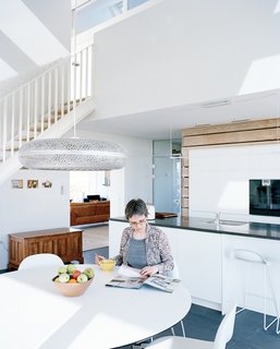 Sophie sits at the Nava dining table in the kitchen, which is flanked by Gubi chairs and illuminated by the Aeros light by Ross Lovegrove for Louis Poulsen.