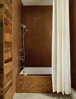 The walls are clad with metal penny tile in the Antique Copper finish from Design and Direct Source of Portland, Oregon. Linear-format tiles in the same finish line the tub.