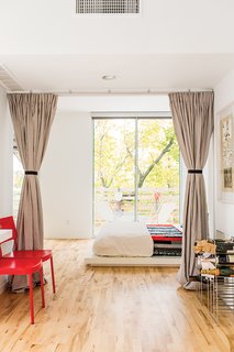 A Versatile House Fulfills All This Musician's Needs - Photo 11 of 11 - The sleeping space is set off with curtains instead of a door to foster an open feel on the ground floor. Bedding from West Elm and a quilt made by Magill’s mother sit atop a platform bed, also from West Elm. The red chairs, originally from Ikea, were another inexpensive secondhand acquisition. The deck chairs feature reversible canvas slings by the fashion designer Julie Brown. 