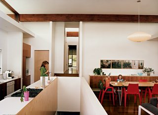 Michele eats lunch in the kitchen; a view of the central hallway and master bedroom lays beyond. Three-year-old Maple slurps from a water bottle with Judith, five, at the dining table, also built by Jamie. The Arco armchairs are by Mario Bellino for Heller, and the Bubble lamp is by George Nelson for Herman Miller. The photograph series is by David Hilliard, titled "That Glorious Society Called Solitude."