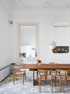 In the dining room, a Poul Henningsen lamp hovers over a table by Philipp Mainzer for E15, surrounded by Hans Wegner Wishbone chairs. The artwork is by Maria Sanchez. The designer added a Banco kitchen by Dada with Jasper Morrison stools.