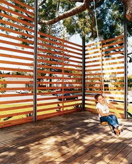 Gabriella swings on the rope swing hung from the podocarpus tree. The twenty-foot-tall, steel-framed, custom-built wood screen provides enough privacy to give the outdoor space the feeling of a room, with the 50-year-old polocarpus tree acting as a roof.
