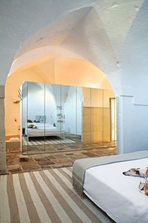 Modern Meets Ancient in a Renovated Italian Vacation Home - Photo 6 of 8 - The house gracefully marries modern and ancient, as seen in the master bedroom, where a custom-built mirrored storage unit divides the sleeping and bathing areas.