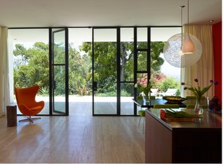 Glass windows wall in the open-concept kitchen-dining spaces of the Sunrise House while glass doors open the spaces out into the garden beyond.
