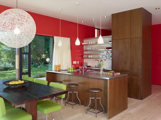Designed to harness the sun, architect Birgitte Hovmøller's vacation house near San Diego features a roof full of solar panels and plenty of space for an extended family to relax. Finished in a dark wood, the kitchen features white metal countertops and shelving. A white pendant light, white sheer curtain and a white wall tie the interior design scheme in with the home's exterior palette.