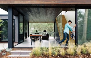 Modern Home Designed for Live Music in Beverly Hills - Photo 1 of 10 - With his son, William, watching, architect Noah Walker tries out the floor-to-ceiling Schüco glass doors he integrated into a guesthouse he designed off an existing barn for Nathan Frankel, an amateur violinist, in Beverly Hills, California. The new portion features an open living-dining area. See more glass houses we love!