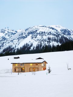 The Strolz House nestles in the winter snow at the edge of the Austrian village of Lech. Large wooden shutters help protect the windows against avalanche damage.