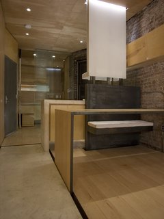 A view of the bathroom and kitchen from the main living area; the front door is at left. At right is the bench of fabricated steel, from Master Kitchen Supplies (212-533-2356). Set into a recess (with Häfele hardware) separating the maple flooring and the concrete ribbon, near left, is a table that can be used for dining, or rolled across the apartment for use as a work surface. Chan left some exposed brick on the load-bearing wall to retain what he could of the apartment’s original character. Image courtesy Brian Riley.