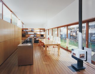 The architects designed the large dining table, which is framed by the open kitchen, the wood-burning stove, and the garden beyond.