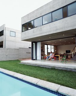 25 Modern Homes That Kill it With Concrete - Photo 8 of 25 - Gregory and Caryn Katz are dwarfed beneath the cantilevered concrete overhang, which houses the bedroom on the upper level. The stackable glass doors that run beneath allow the house to open completely to the yard and swimming pool, soften the severity of the concrete, and blur the boundary between indoors and out.