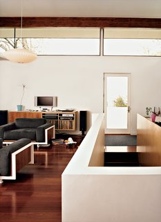 In the main living space, stairs lead to the basement. The white-framed chairs and couch were built by Jamie; the cabinets were designed by Jamie and built by a local cabinetmaker. Brazilian cherry floors run throughout the main house. The clerestory windows allow light in without sacrificing privacy.