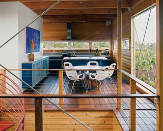Lava Flow 4, The Big Island - Photo 4 of 9 - The home's upper floor features copious amounts of untreated pine. Five large cross-braces keep the timber frame rigid. The royal blue Ikea kitchen, Noguchi Cyclone dining table for Knoll, and Karim Rashid Oh chairs for Umbra all made the trip from the mainland in a twenty-foot-long shipping container. Above the wall-mounted credenza, a colorful painting of the Puma moonrise is by local artist Arthur Johnson.