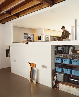 The couple’s living room (which includes a flat-screen TV) overlooks Tad Beck’s studio; art supplies are stored in niches that are invisible from the living space above. A hallway along the edge of the building provides an alternate route to the front door.